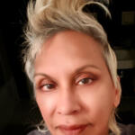 Close-up of a person with light blonde, styled hair, neutral expression, and makeup.
