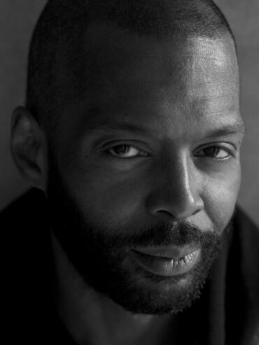 Close-up portrait of a man with a shaved head and beard in black and white.