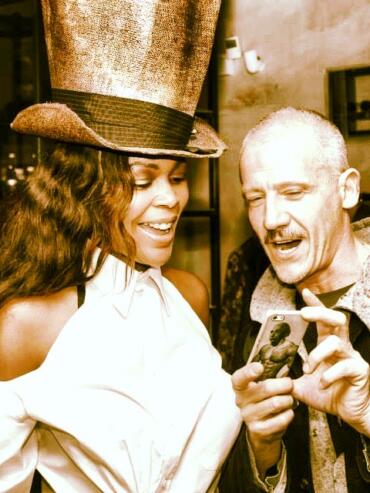 Two friends sharing a joyful moment, one wearing a large top hat with a vintage vibe.