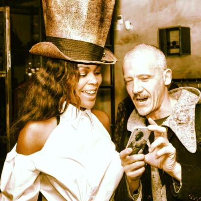 Two friends sharing a joyful moment, one wearing a large top hat with a vintage vibe.