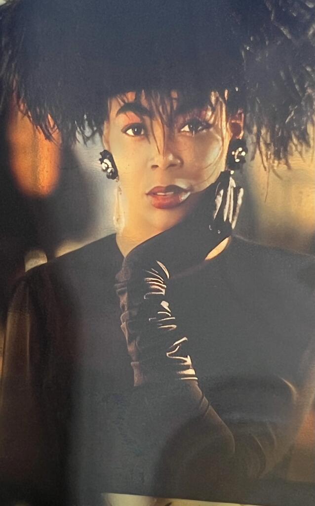 Elegant woman with voluminous curly hair, wearing stylish earrings and black gloves.