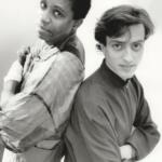 Black-and-white photo of two men standing back-to-back with arms crossed, showcasing casual fashion styles.