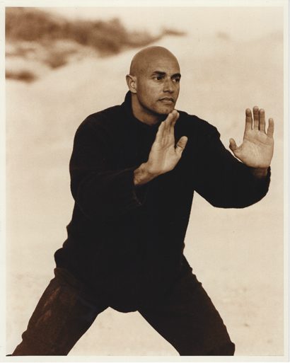 Sepia-toned image of a man in a black sweater practicing martial arts stance outdoors.