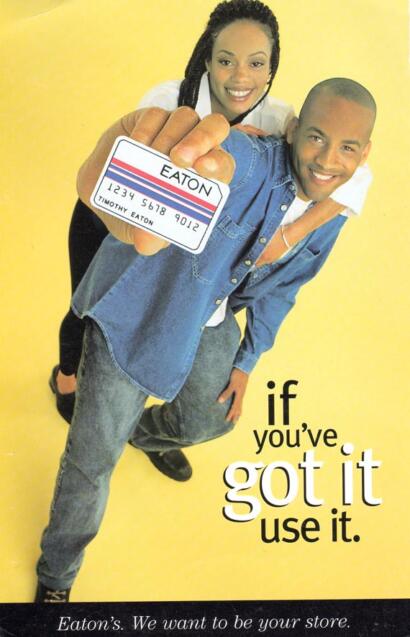 Young man holding a store card, smiling, with a woman behind him, yellow background, promotional message.