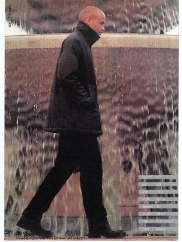 Man walking in wetsuit with water spray and cityscape background, stylish and modern.