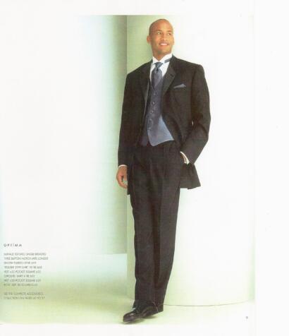 Man in a tailored black tuxedo with a vest and tie, posing against a light background.