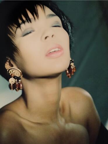 Close-up of a woman with short black hair, wearing ornate gold and red earrings, with a serene expression.