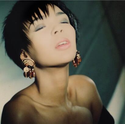 Close-up of a woman with short black hair, wearing ornate gold and red earrings, with a serene expression.