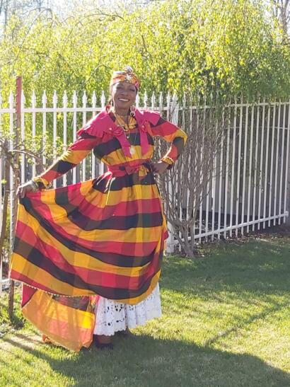 Woman standing outdoors in a colorful, striped dress with a white lace underskirt, smiling.