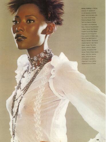 Model with bold makeup wearing layered silver jewelry and a white ruffled blouse.