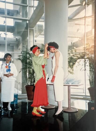 Women during a fashion show: one adjusting another's headwear in a bright, modern space.