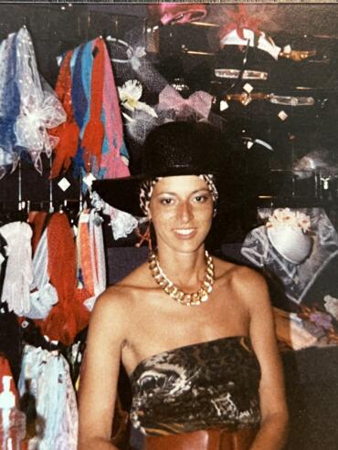 A woman in a strapless animal print top and black hat with a leopard-print band, accessorized with a chunky gold necklace, inside a boutique.