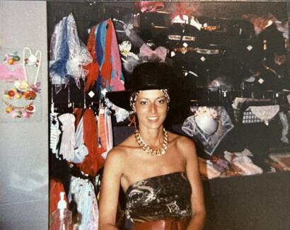 A woman in a strapless animal print top and black hat with a leopard-print band, accessorized with a chunky gold necklace, inside a boutique.