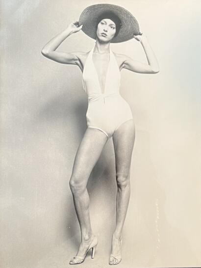 A black-and-white fashion portrait of a woman in a vintage swimsuit, wide-brimmed hat, and heels.