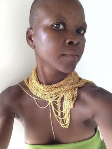 Close-up of a woman with short hair wearing layered gold necklaces and a green strapless top.
