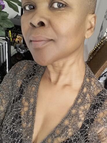 Close-up of a woman with a shaved head wearing a sparkly, patterned top.