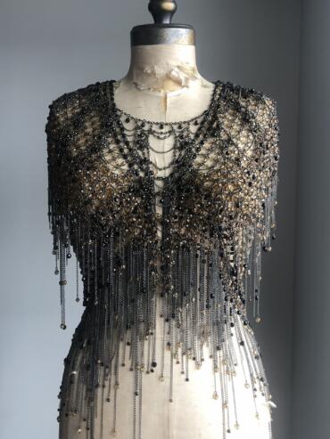 Beaded black and gold garment displayed on a vintage dress form against a neutral background.