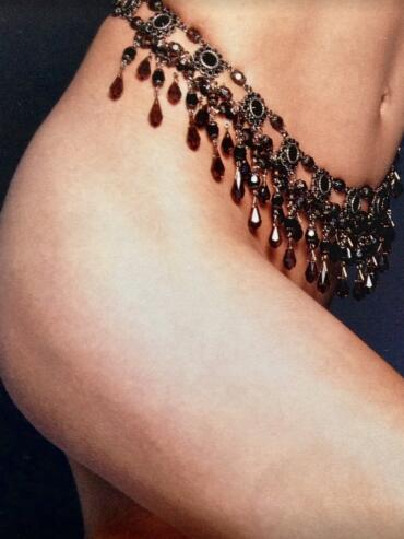 Close-up of a glamorous black and red gemstone fringe jewelry piece draped over a bare shoulder and arm.