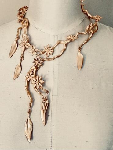 Elegant rose gold floral necklace with leaf accents displayed on a dress form.