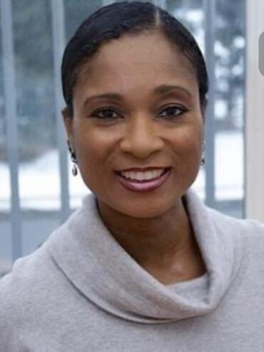 Close-up of a woman smiling, wearing a light gray cowl neck sweater, with a blurred wintery background.