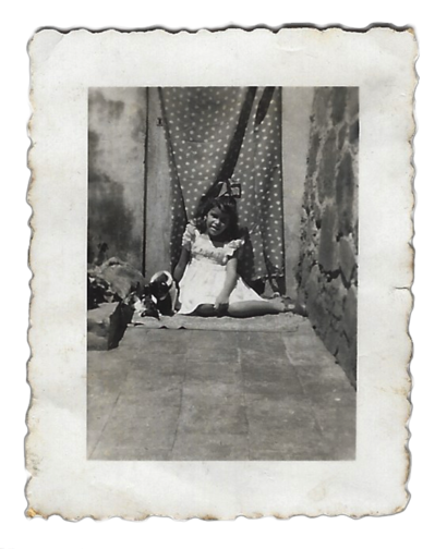 Young girl in a dress sitting on a porch step, with a polka-dot curtain backdrop.