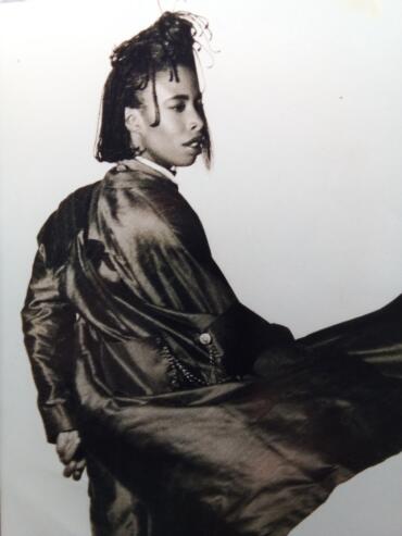 Black-and-white portrait of a woman with short dreadlocks, wearing a shiny, satin-like jacket.