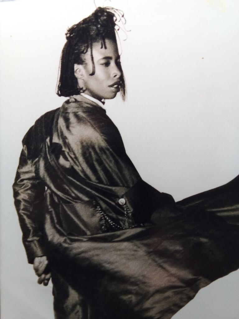 Black-and-white portrait of a woman with short dreadlocks, wearing a shiny, satin-like jacket.