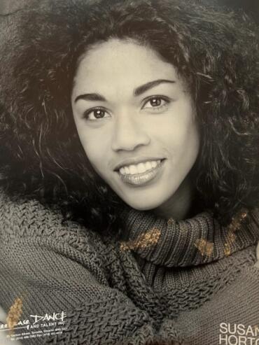Black-and-white portrait of a woman with curly hair, smiling and wearing a knitted turtleneck.