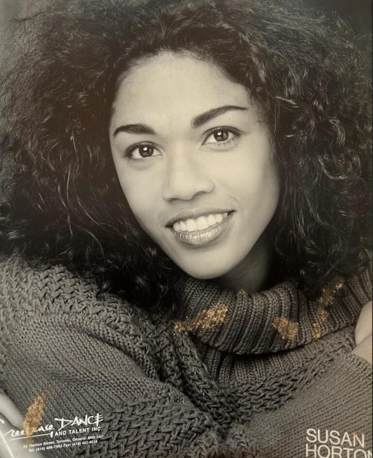 Black-and-white portrait of a woman with curly hair, smiling and wearing a knitted turtleneck.