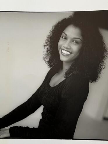 Portrait of a smiling woman with curly hair, wearing a black top, in a black and white photograph.