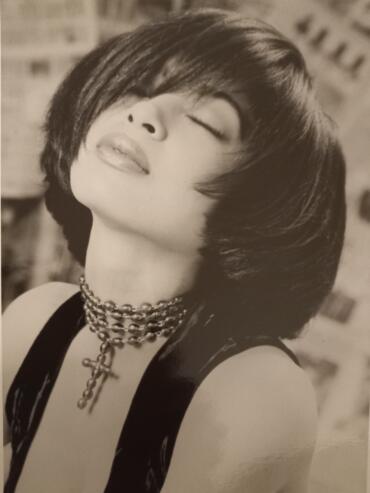 Black and white portrait of a woman with short, sleek hairstyle and layered bangs, wearing layered necklaces.