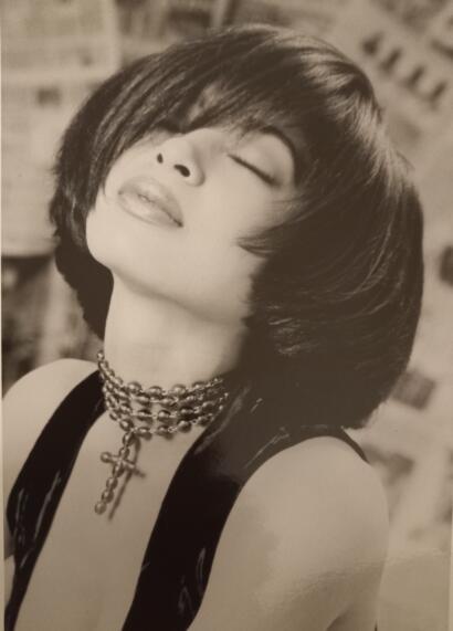 Black and white portrait of a woman with short, sleek hairstyle and layered bangs, wearing layered necklaces.