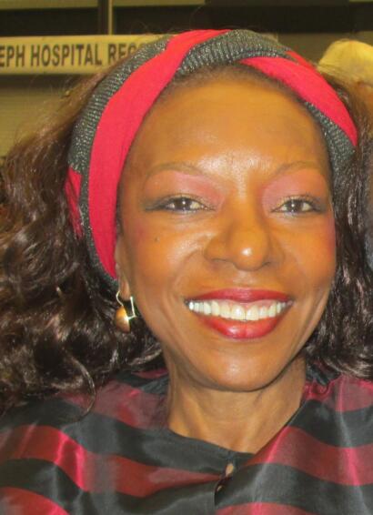 Smiling woman in colorful headscarf and striped attire at a hospital reception area.
