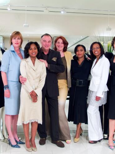 Group of women and one man in stylish business attire inside a clothing store.