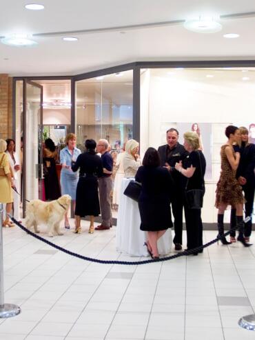 Group of elegantly dressed people mingling at a fashion event in a shopping mall.