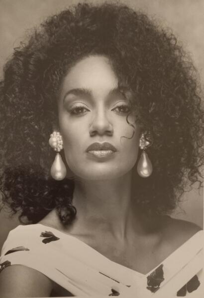 Black-and-white portrait of a woman with voluminous curly hair, elegant earrings, and a floral dress.