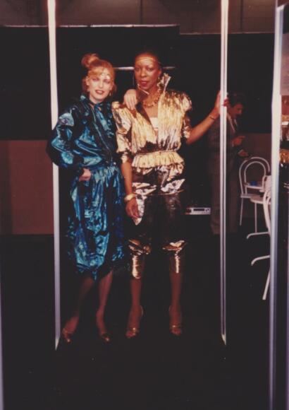 Two women in glamorous, metallic fashion poses at an event.
