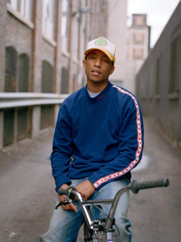 Young man wearing a blue sporty sweatshirt, sitting on a bicycle in an urban alleyway.