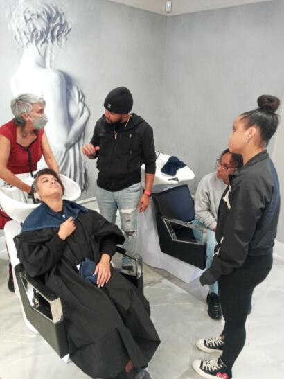 Group of people in a salon, with a woman receiving a hair treatment at the wash basin.
