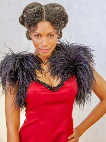 Woman in a red dress with feathered black shoulder accents, styled in vintage-inspired hair.