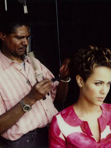 Hairstylist applying makeup to a woman's short, styled hair in a professional salon setting.