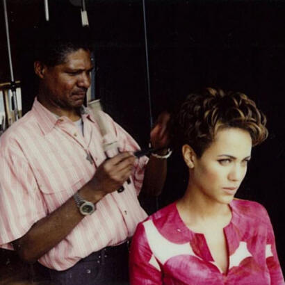 Hairstylist applying makeup to a woman's short, styled hair in a professional salon setting.
