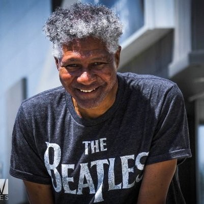 Smiling man with curly gray hair wearing a black "The Beatles" t-shirt.