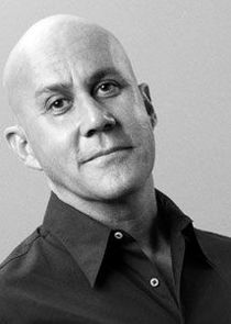 Black and white portrait of a confident, bald man wearing a collared shirt.