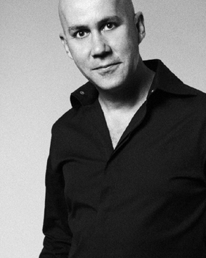Black-and-white portrait of a man in a collared shirt, gazing confidently at the camera.
