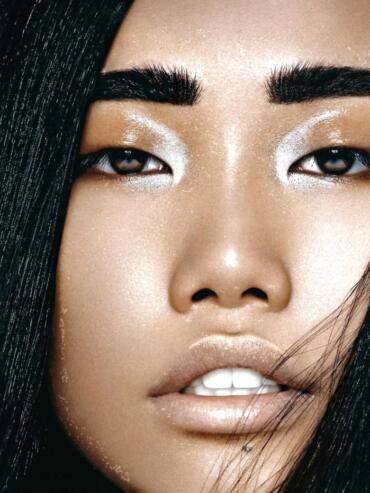 Close-up of a woman's face showcasing glamorous makeup with shimmering eyeshadow and glossy lips.