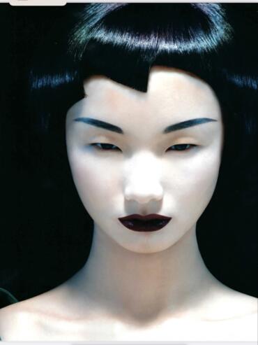 Close-up of a model with dark lipstick and sharp bangs, showcasing modern makeup and hairstyle.