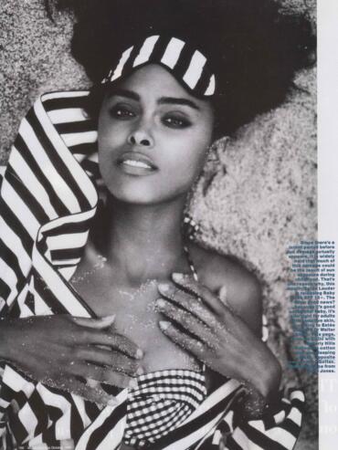 Black and white photo of a woman laying on sand, wearing striped clothing and a patterned headscarf.