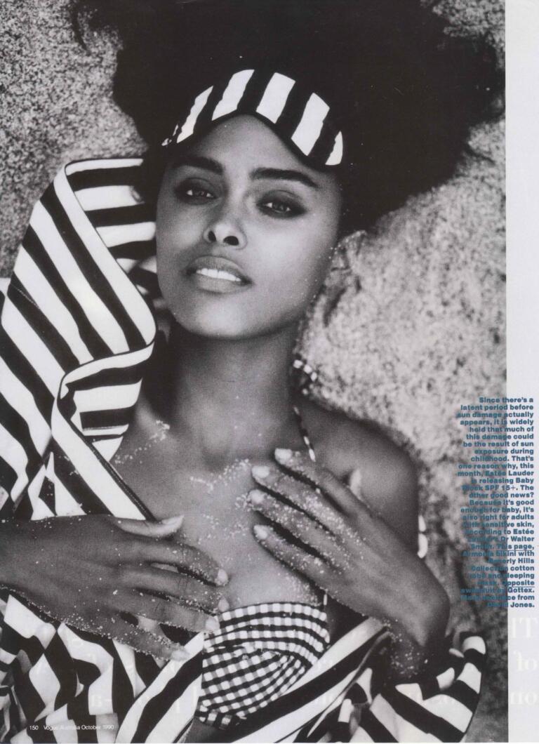 Black and white photo of a woman laying on sand, wearing striped clothing and a patterned headscarf.