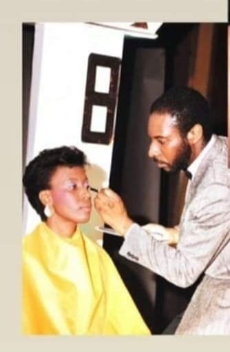 A makeup artist applying makeup to a woman in a yellow cape.